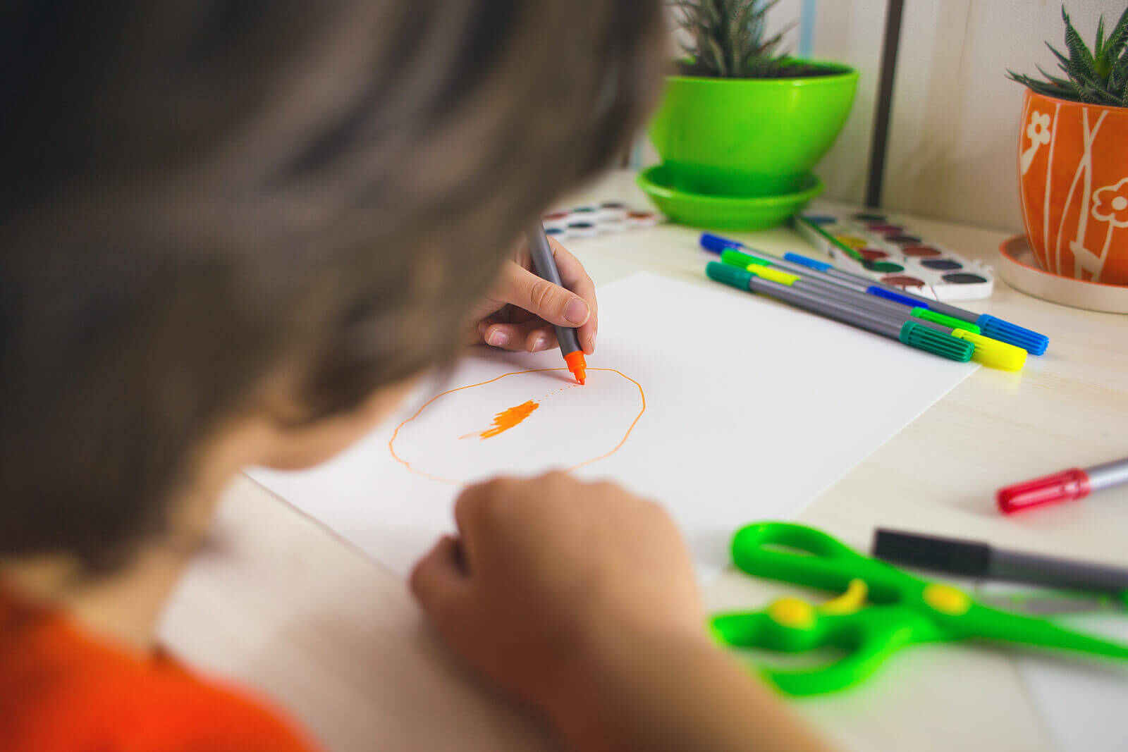 The boy draws with felt-tip pens on paper, the child is engaged in creativity, the child does his homework, left-handed day