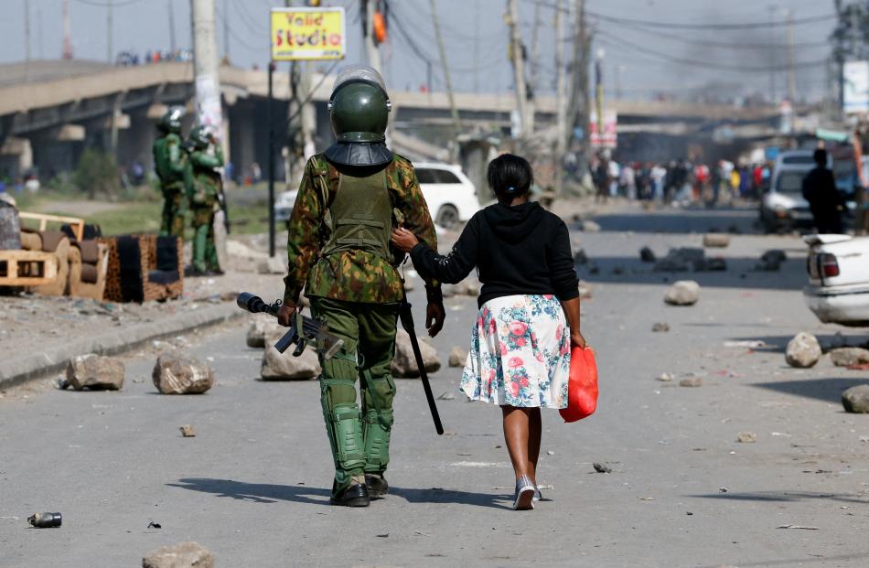 A woman walks next to a riot police officer, during an anti-government demonstration, in Nairobi,...