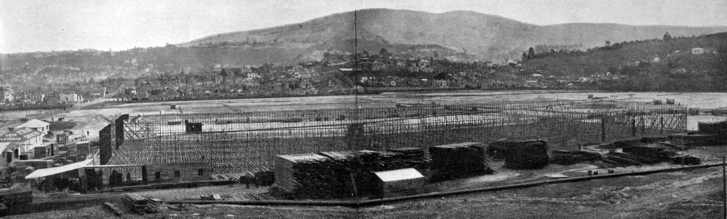 The wooden frame of the first block of the exhibition buildings at Logan Park dwarfs stacks of...