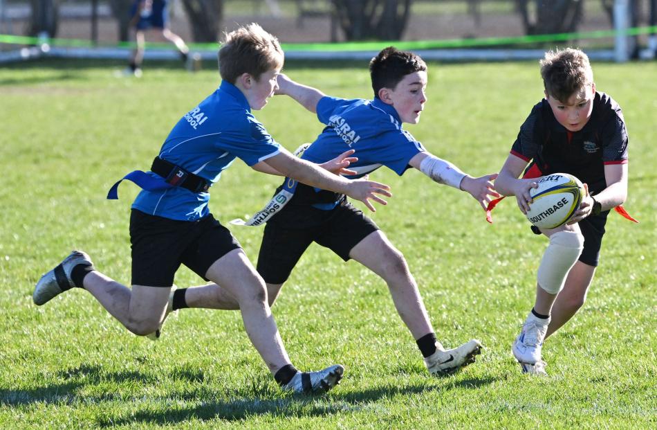 Harrison Tapp, 11, of Silverstream School tries to avoid Kaikorai School defenders Hugo Scott, 10...