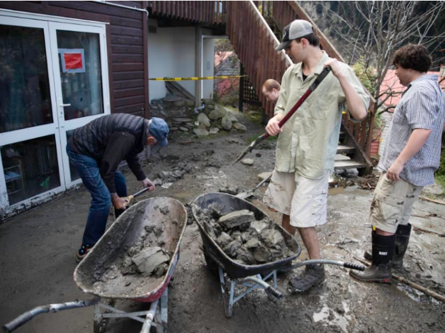 Jasper Thompson, middle right, shovels debris into a wheelbarrow as residents of Reavers Lane,...