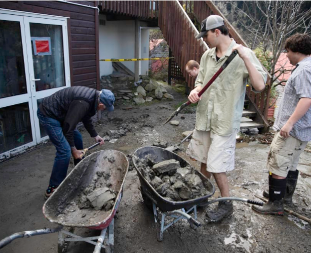 Jasper Thompson, middle right, shovels debris into a wheelbarrow as residents of Reavers Lane,...